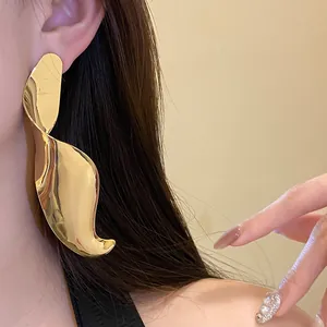 Close-up of large geometric twisted gold earrings with a minimalist luxury style