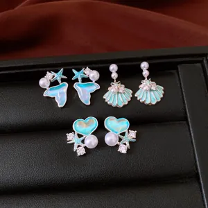Detail of teal enamel shell, mermaid tail, and heart earrings with pearls and zircons