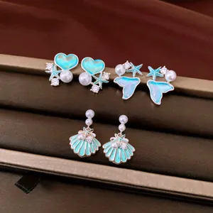 Close-up of ocean-themed earrings set with blue enamel, pearls and zircon on display box