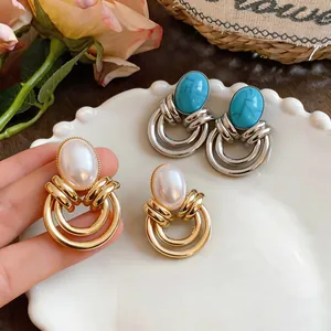 Dettaglio di orecchini vintage in turchese e perla su un piatto decorativo bianco