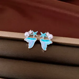 Macro detail of elegant blue mermaid tail and starfish earrings featuring pearls and zircons