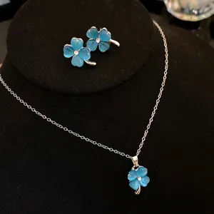 Close-up of blue cat's eye four-leaf clover necklace and earring set on black stand