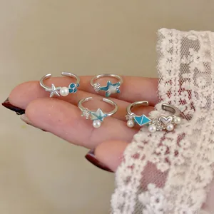 Detail shot of sea-themed open rings with starfish shells pearls and blue enamel accents