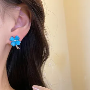 Detailed close-up showing a delicate four-leaf clover ear stud with blue cat-eye stone