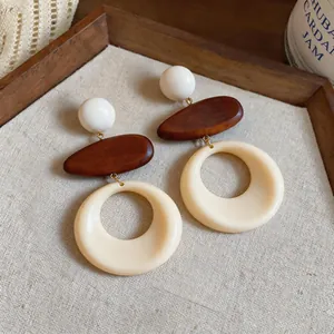 Dettaglio macro di orecchini vintage con elementi in legno marrone e cerchi in resina crema