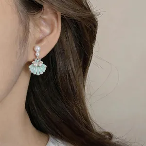Close-up detail of a mint green enamel shell earring with pearls worn on a female ear
