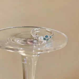 Close-up detail of silver starfish and pearl open ring with blue enamel shell design