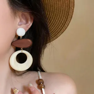Primo piano di orecchini oversize retrò con elementi in legno e resina crema sulla modella