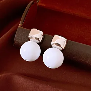 Elegantes pendientes colgantes vintage de resina blanca con aguja de plata en fondo marrón.