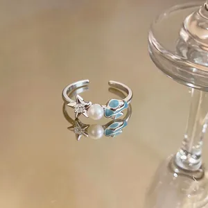 Close-up of open ring featuring a zircon starfish, pearl and blue enamel shell.