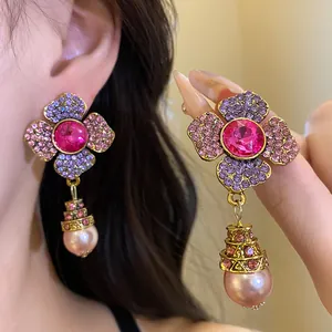 Dettaglio macro di orecchini a fiore vintage con strass rosa e pendente di perla