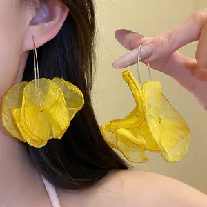 Detail of large yellow chiffon flower drop earrings worn by a model and held in hand.