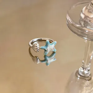Close-up of a silver starfish and shell open ring with light blue enamel and zircons