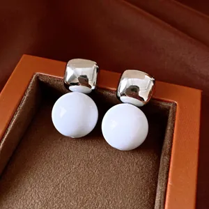Primer plano de pendientes cuadrados plateados y esferas de resina blanca en un joyero.