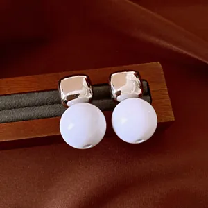 Primer plano de pendientes geométricos con cuadrados plateados y esferas de resina blanca.