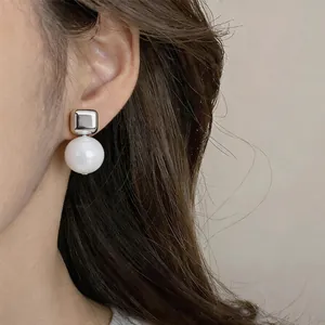 Pendiente de botón cuadrado de plata con una gran perla de resina blanca en la oreja.
