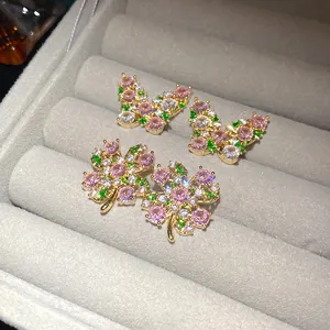 Detailed view of pink and green zircon butterfly and clover earrings in a gray box