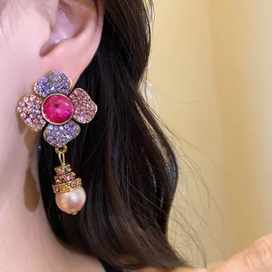 Dettaglio ravvicinato di orecchini a fiore vintage con cristalli rosa e una perla pendente