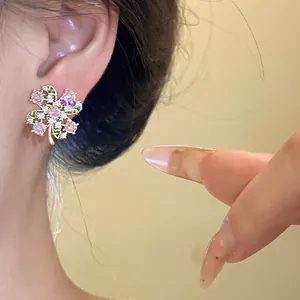 Close-up of sparkling clover-shaped earring with pink and green zircons on a model's ear
