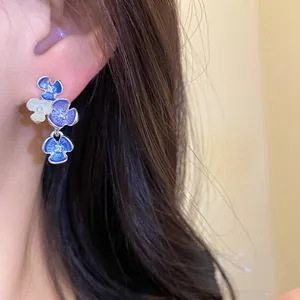 Dettaglio ravvicinato di orecchini a lobo con fiori blu e bianchi e strass sull'orecchio