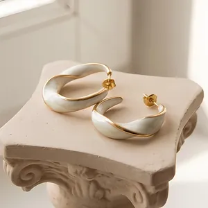 Dettaglio di alta qualità di orecchini a C intrecciati placcati in oro 18K con smalto bianco.