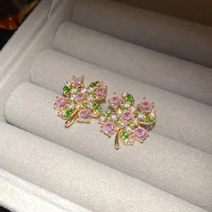 Macro view of gold-tone four-leaf clover stud earrings with sparkling pink zircons