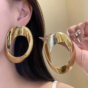 Close-up of oversized geometric hollow gold earrings with glossy metallic finish.
