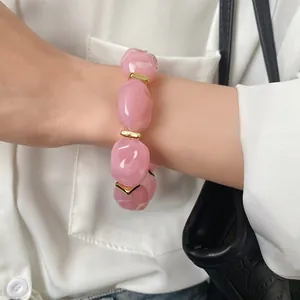 Close-up detail of a chunky irregular pink acrylic bracelet with stylish gold-tone metal spacers