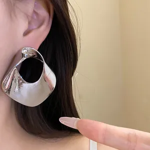 Close-up detail showing the metallic texture of a large silver geometric hollow earring