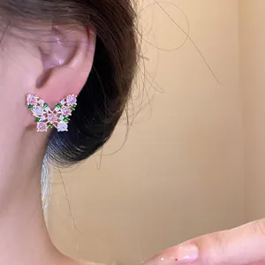 Detail shot of a sparkling butterfly stud earring with pink and green stones.
