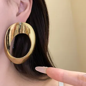 Close-up shot of a large chunky gold geometric hollow hoop earring worn on an ear