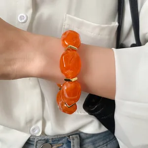 Close-up of an orange irregular acrylic bead bracelet with gold accents on wrist