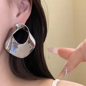 Macro view of a large geometric hollowed silver stud earring worn on model's ear