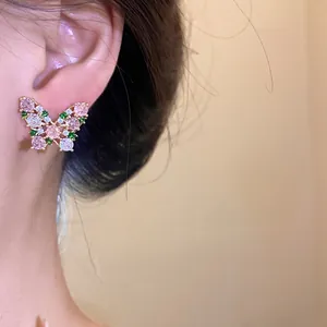 Detailed view of elegant gold-toned butterfly earrings with pink and green stones