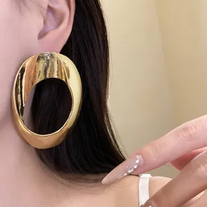 Close-up of large minimalist golden hollow geometric earrings on a model