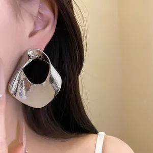 Detailed view of large silver-tone geometric hollow earrings worn by a fashion model