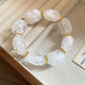 Close-up of irregular white acrylic beads with golden metal spacers on a bracelet