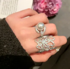 Close-up detail of hollow floral zircon ring and pearl ring worn on a hand, luxury style.