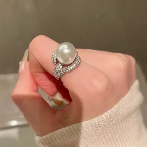 Detailed view of an elegant pearl open ring with sparkling zircon accents on a finger