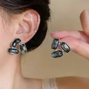 Boucles d'oreilles élégantes avec cristaux gris foncé portées à l'oreille et à la main