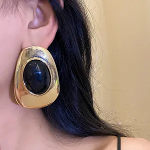 Close-up detail of vintage gold-tone metal and black resin oval stud earring