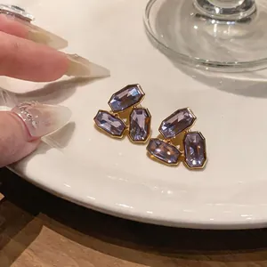 Vue détaillée de boucles d'oreilles dorées avec des cristaux violets de taille émeraude