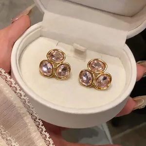 Gros plan de boucles d'oreilles dorées avec trois cristaux roses étincelants en boîte