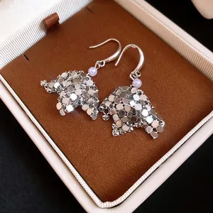 Macro view of silver scale-like sequin drop earrings with a purple pearl in a luxury box.