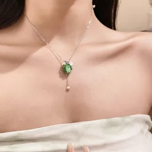 Close-up detail of a stainless steel necklace with green resin grape pendant and pearls