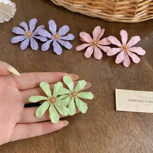 Primo piano di grandi orecchini a fiore verde chiaro con petali pieghettati e centro oro.