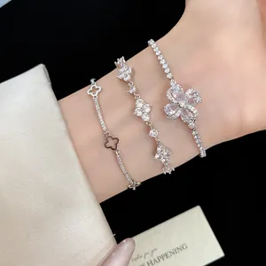 Primo piano di tre eleganti bracciali con quadrifoglio e fiori in zircone argento sul polso.