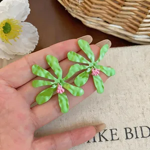 Dettaglio ravvicinato di orecchini a fiore plissettati verdi con accenti floreali in smalto rosa
