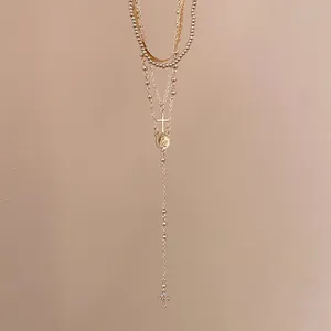 Close-up of a gold layered cross necklace with rhinestone pendant and vintage medallion.
