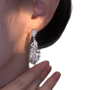 Elegant silver feather drop earrings with micro-pave cubic zirconia shown on model's ear.